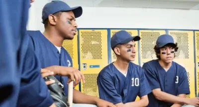 High school baseball players in uniform sitting together in a locker room